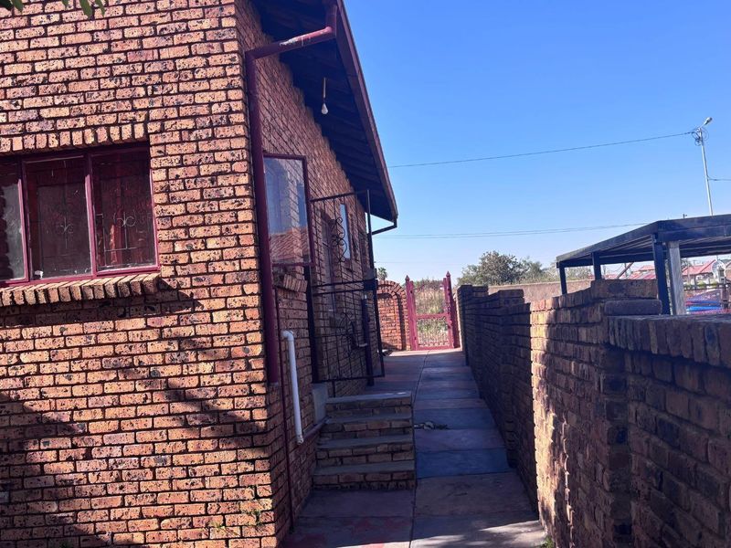 A side view of the property featuring face brick exterior walls, a paved walkway, and a secure brick boundary wall.