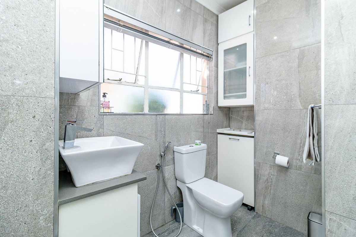 Modern bathroom featuring grey tiled walls and flooring, a vessel sink with vanity storage, a toilet with bidet spray, and built-in wall cabinetry.