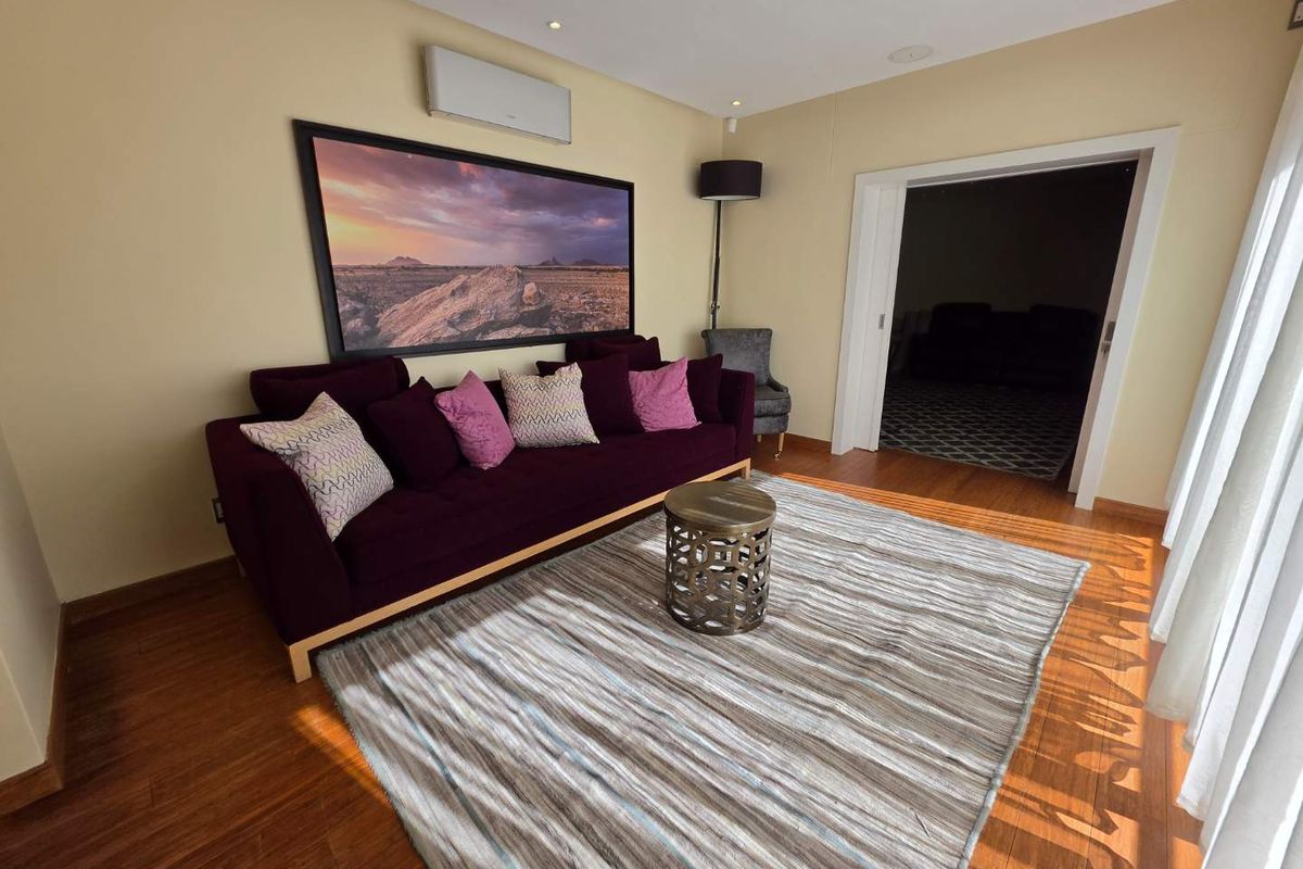 A well-maintained living room featuring polished timber flooring, recessed ceiling lighting, and a wall-mounted air conditioning unit.