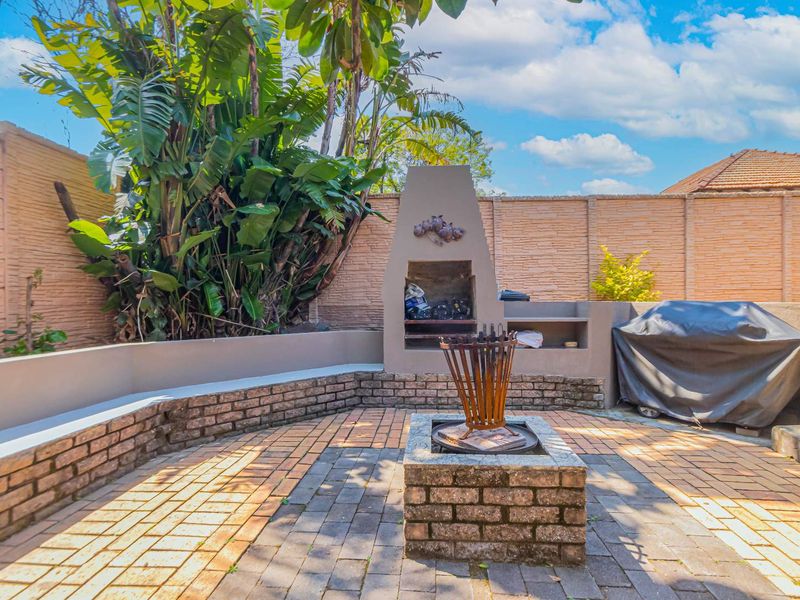 Outdoor entertainment area featuring a built-in braai, central fire pit, and brick-paved patio enclosed by a perimeter wall.