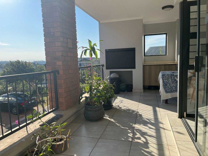 Covered balcony featuring a built-in braai, tiled flooring, and a brick pillar, offering an outdoor entertainment space with views.