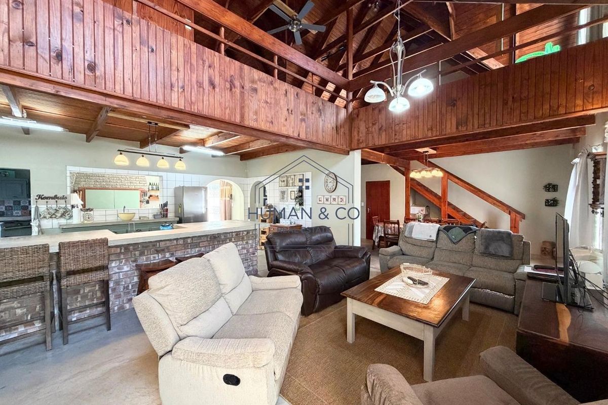 Spacious open-plan living area featuring a double-volume timber ceiling, mezzanine level, and a rustic brick breakfast bar connecting to the kitchen.