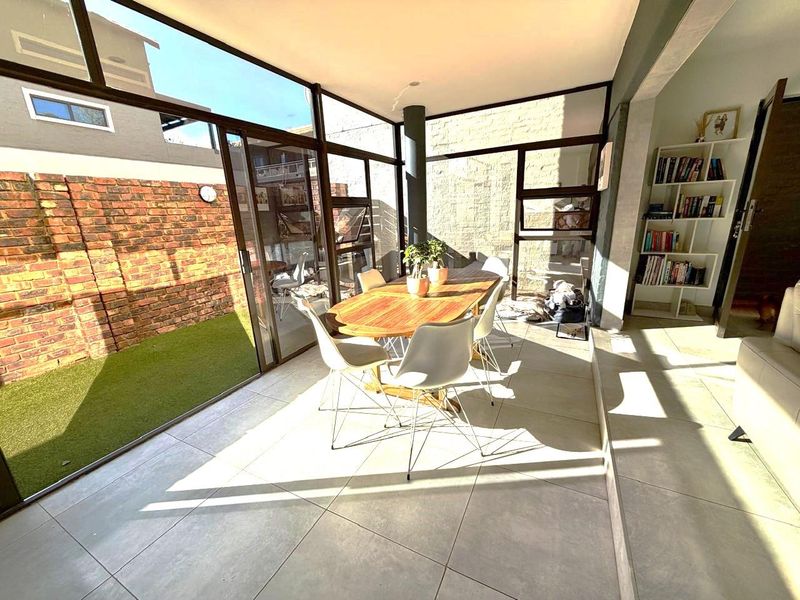 Bright, enclosed patio area featuring large glass sliding doors, tiled flooring, and a stone feature wall, seamlessly connecting the interior to the rear garden.
