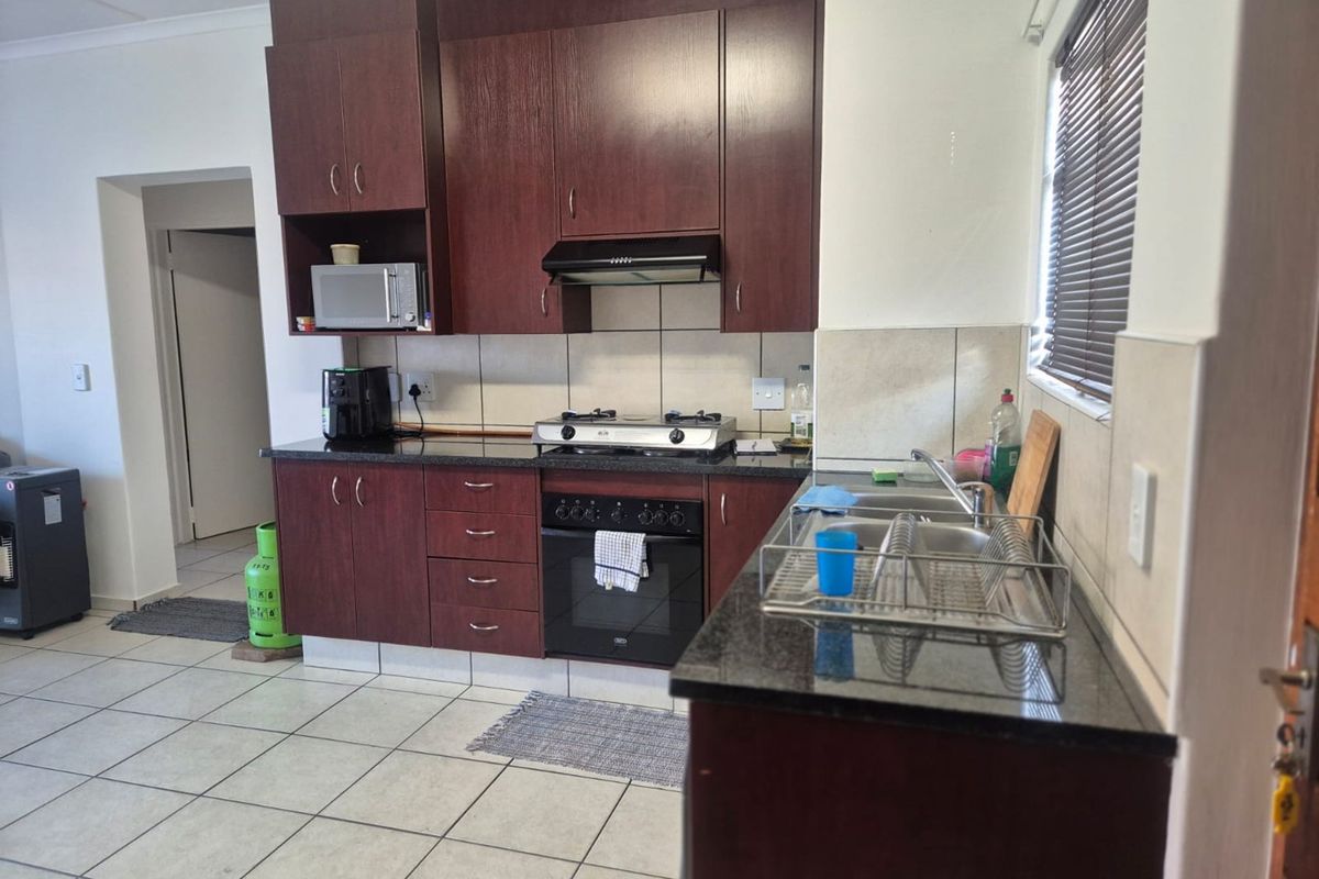 Functional kitchen featuring dark wood cabinetry, granite countertops, built-in oven with gas hob, extractor fan, and a double bowl stainless steel sink.