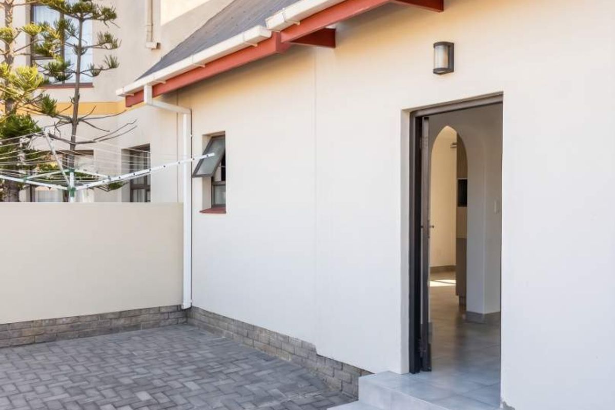 A view of the rear exterior area featuring paved courtyard, white rendered walls, red roof trim, and a direct entrance into the home.