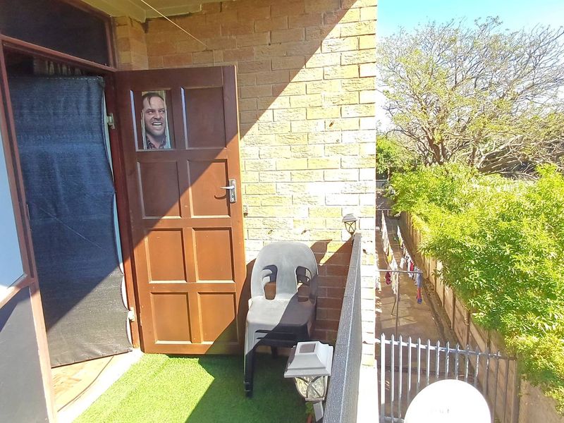 A small balcony area featuring a brick facade, timber door, and metal railing overlooking a garden space.