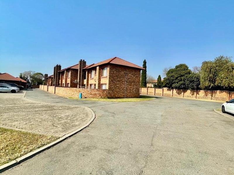 Exterior view of a face-brick cluster complex featuring a tiled roof, paved driveway, and perimeter boundary wall within a residential estate.