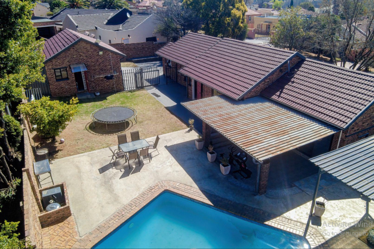 Aerial view of the property featuring a swimming pool, paved patio area with covered roofing, and a spacious backyard.