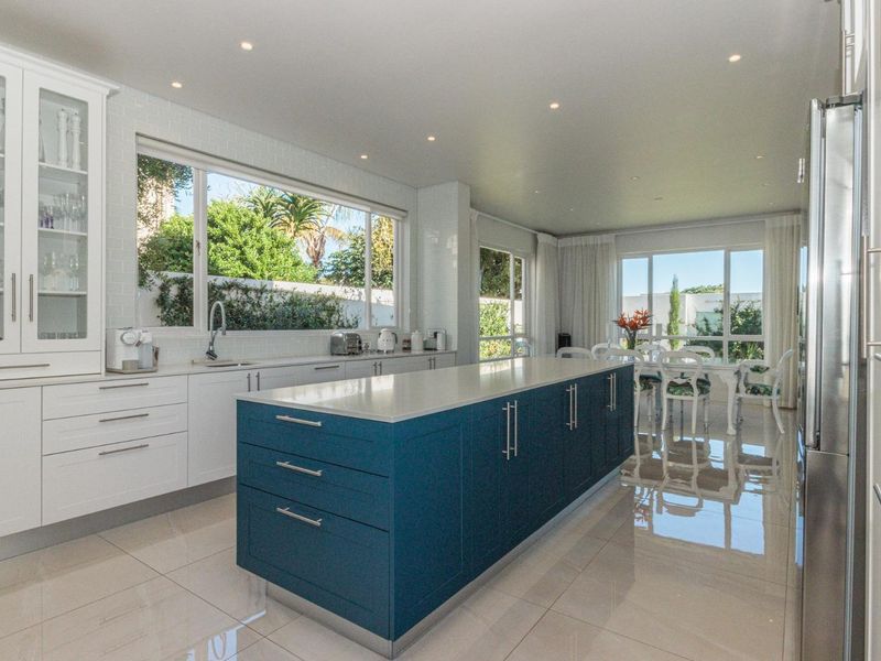 Modern open-plan kitchen featuring a large blue central island, white cabinetry, stone countertops, and polished tiled flooring with abundant natural light.