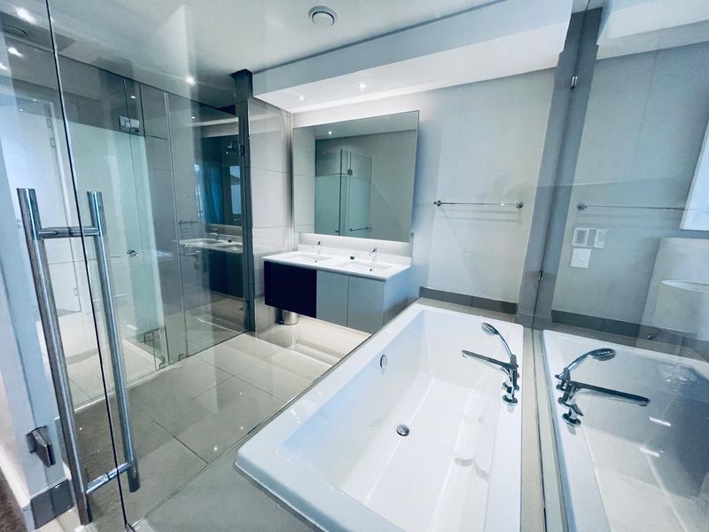 Modern bathroom featuring a double vanity, glass-enclosed shower, and a sleek freestanding bathtub with high-quality finishes and recessed lighting.