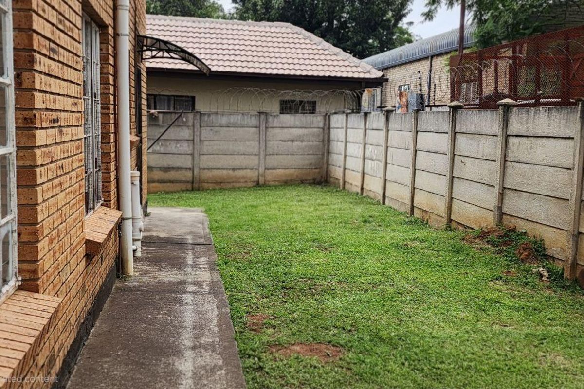 A private rear garden area featuring a concrete pathway, lawn space, and secure perimeter boundary walling.