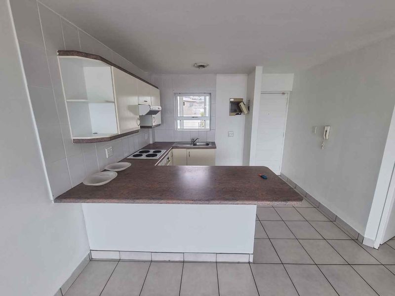 A functional kitchen featuring built-in cabinetry, a laminate breakfast bar, electric hob, and tiled flooring in an open-plan layout.