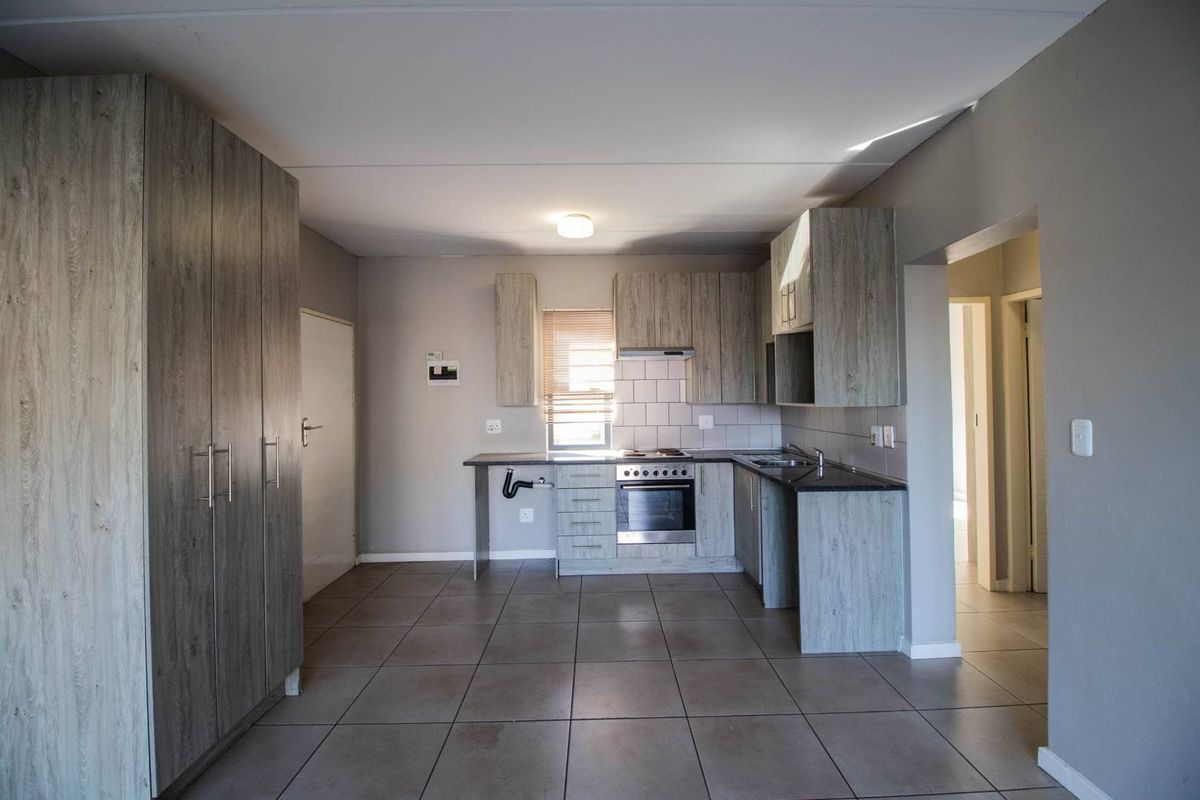 A functional kitchen featuring wood-look cabinetry, tiled flooring, a built-in oven and hob, and a dedicated space for a dishwasher or washing machine.