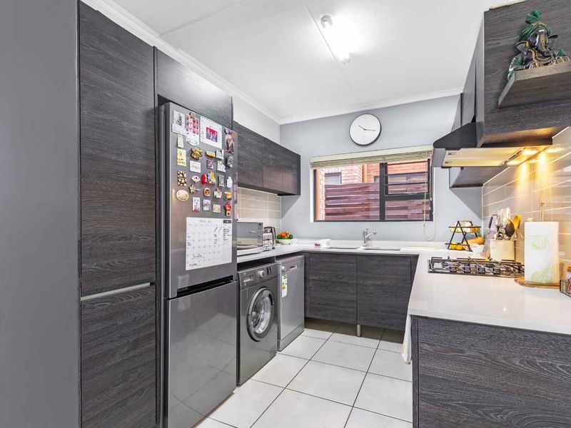 Modern kitchen featuring dark wood cabinetry, stone countertops, a gas hob, extractor fan, and tiled flooring with integrated appliance space.