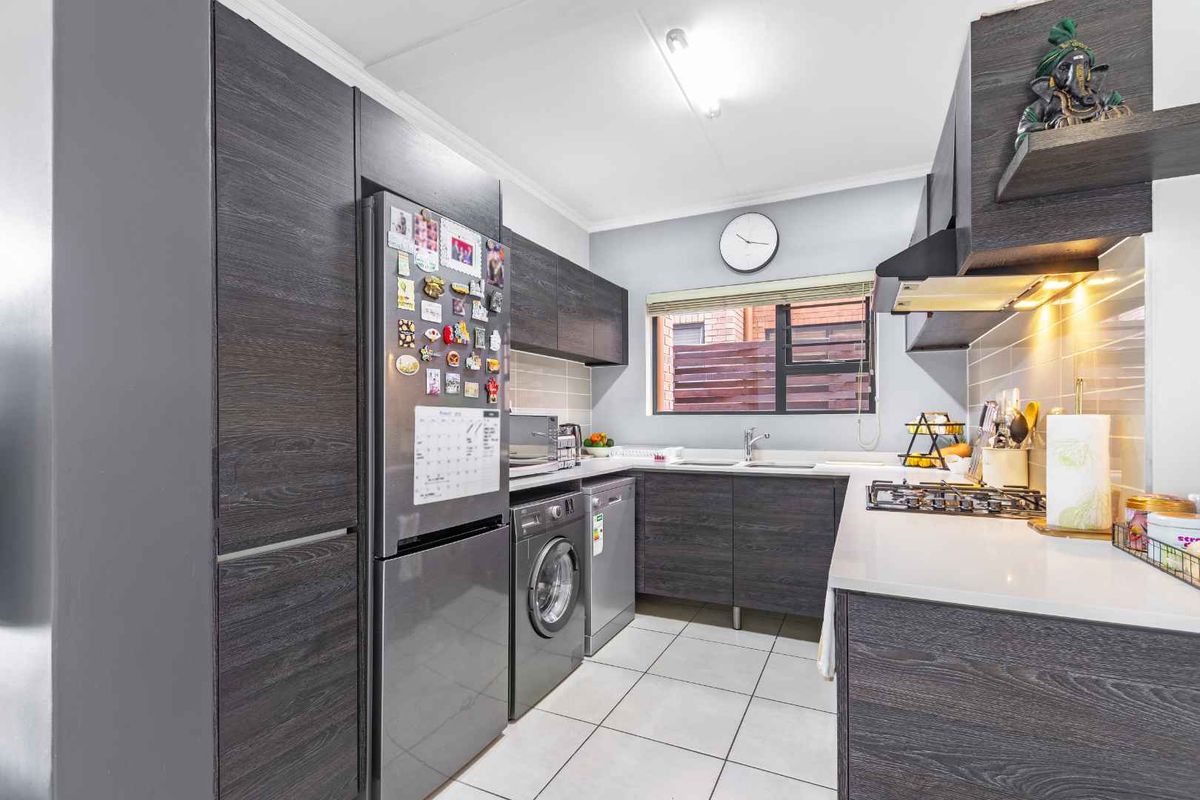 Modern kitchen featuring dark wood cabinetry, stone countertops, a gas hob, extractor fan, and tiled flooring with integrated appliance space.