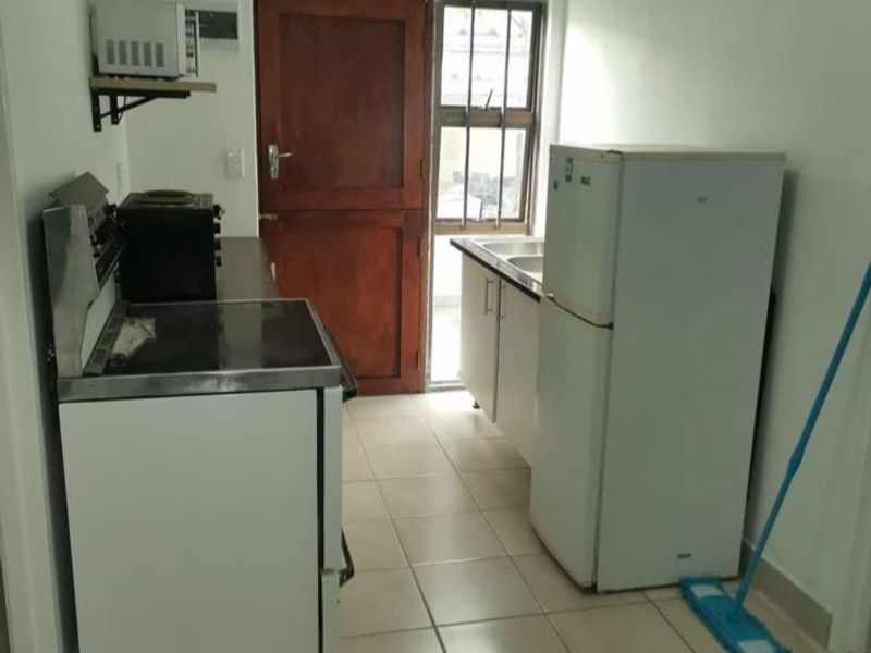 A compact kitchen featuring tiled flooring, basic base cabinetry, a sink, and an electric stove, with direct access to an exterior door.