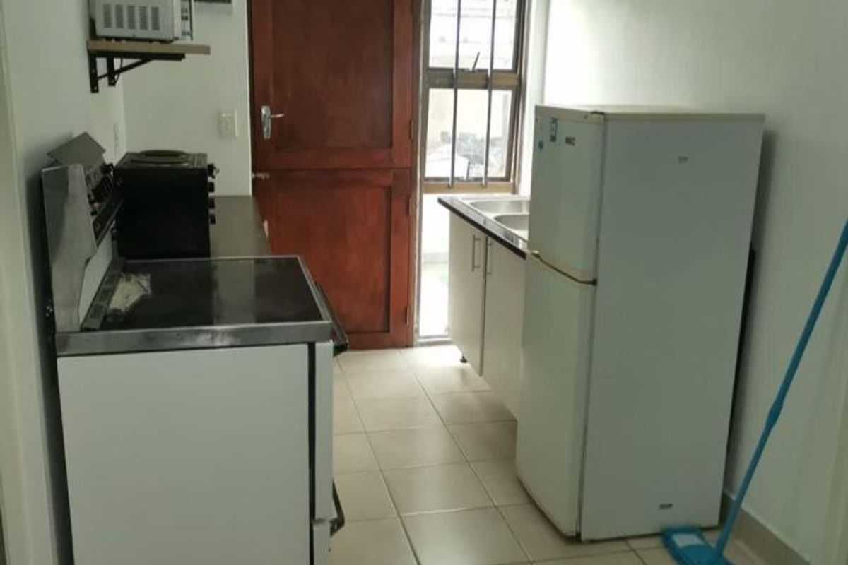 A compact kitchen featuring tiled flooring, basic base cabinetry, a sink, and an electric stove, with direct access to an exterior door.