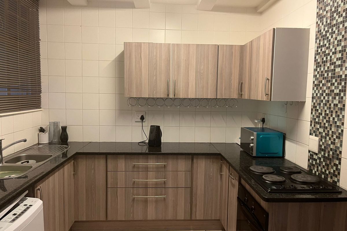 A functional kitchen featuring wood-look laminate cabinetry, granite countertops, a built-in electric hob and oven, and a decorative mosaic tile feature wall.