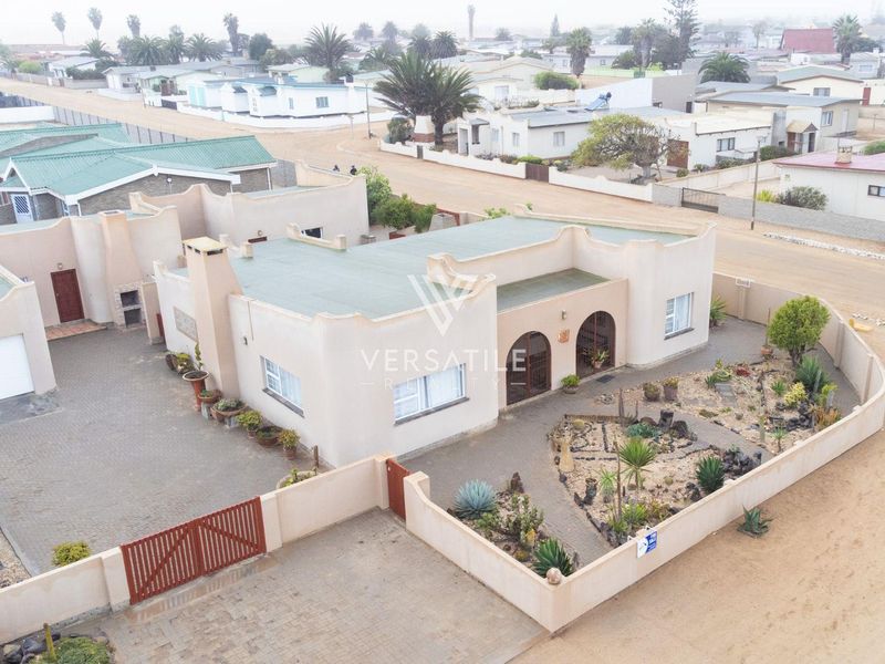 Aerial view of a residential property featuring a paved driveway, gated entrance, and a landscaped garden with established desert-style plantings.