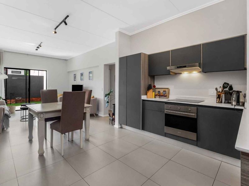 Modern open-plan living area featuring a sleek kitchen with dark cabinetry, integrated appliances, and tiled flooring, flowing seamlessly into the dining and lounge space.