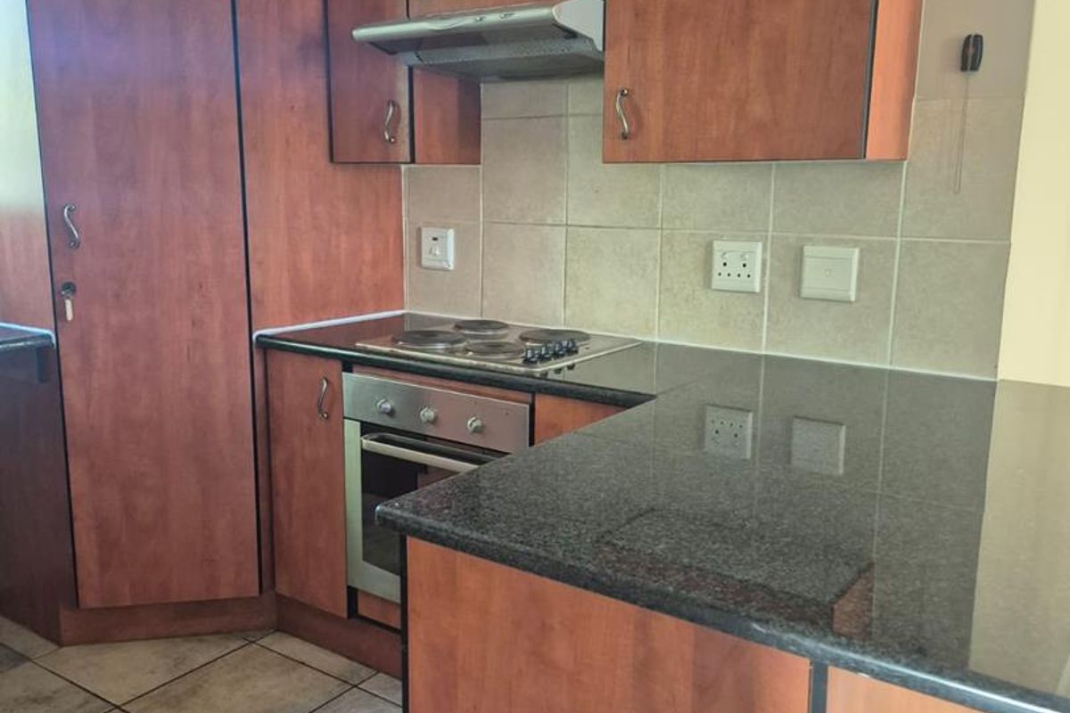A functional kitchen featuring wood-finish cabinetry, dark granite countertops, a built-in oven, electric hob, and extractor fan with tiled flooring.