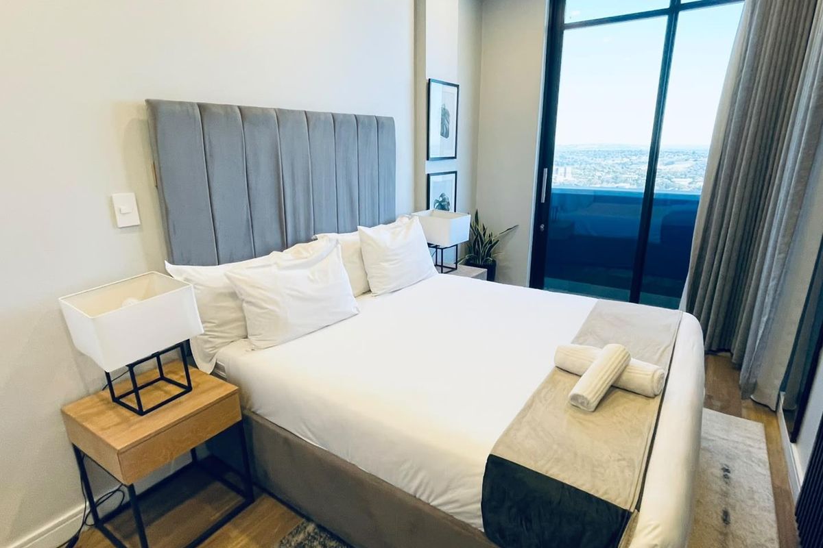 Modern bedroom featuring floor-to-ceiling windows with expansive city views and access to a private balcony.