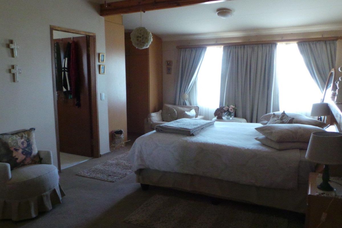 A spacious bedroom featuring built-in cabinetry, neutral carpeting, and large windows with curtains, providing a comfortable and functional living space.