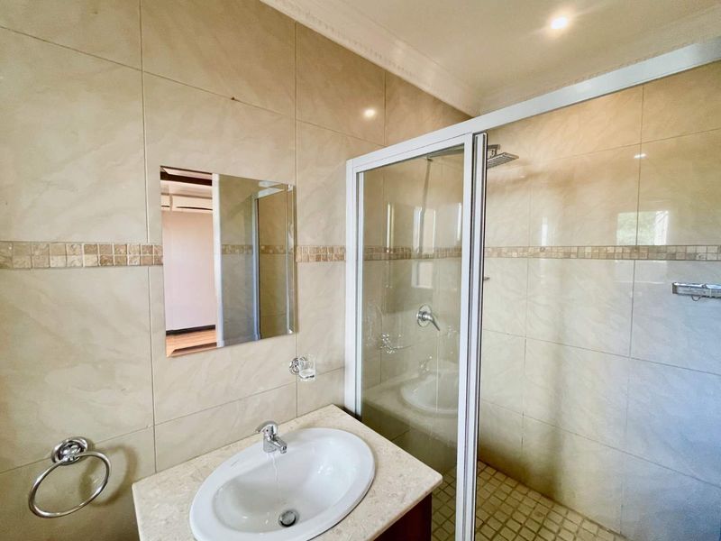 A clean, functional bathroom featuring a glass-enclosed shower, vanity basin with chrome fixtures, and neutral wall tiling.