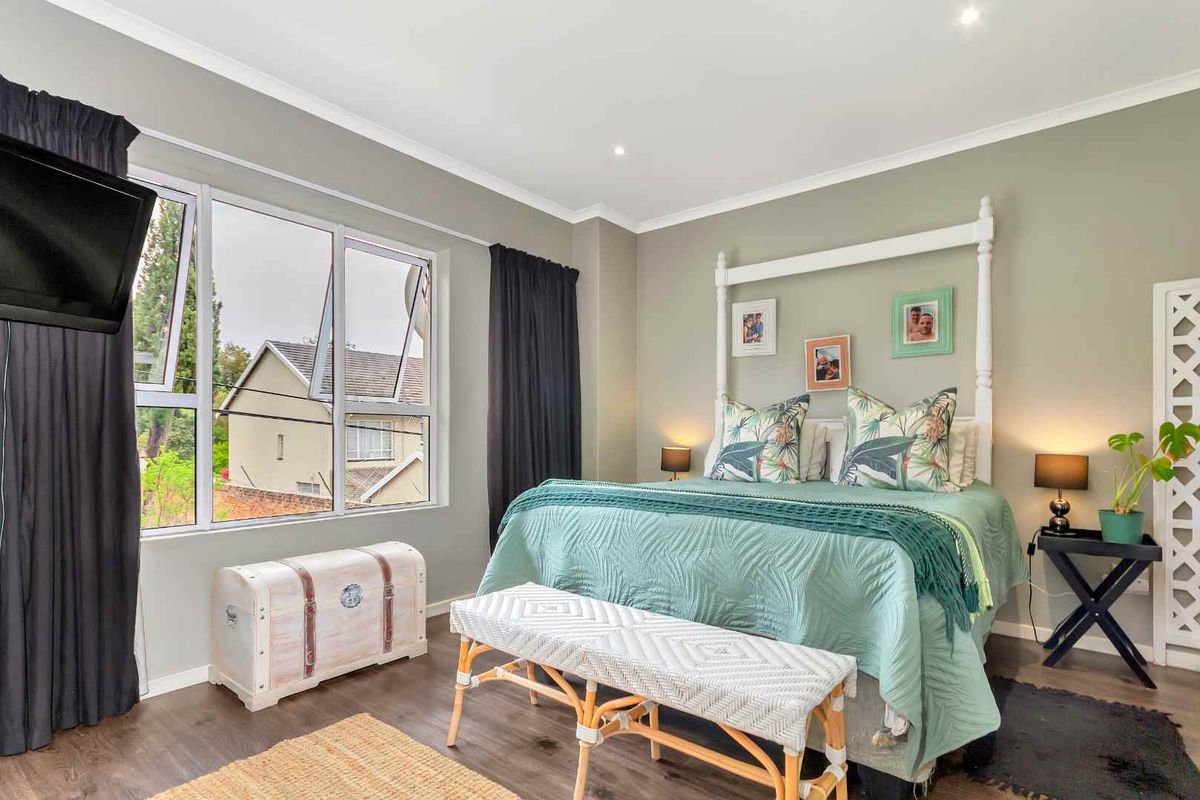 A well-maintained bedroom featuring large windows, laminate flooring, and neutral wall tones, offering a comfortable and bright living space.