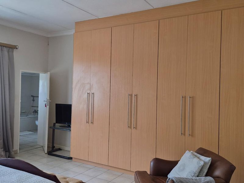 A bedroom featuring extensive floor-to-ceiling built-in wooden cupboards, tiled flooring, and an adjoining en-suite bathroom.