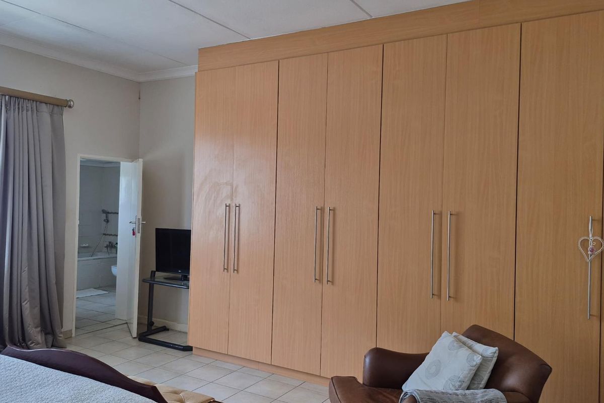 A bedroom featuring extensive floor-to-ceiling built-in wooden cupboards, tiled flooring, and an adjoining en-suite bathroom.