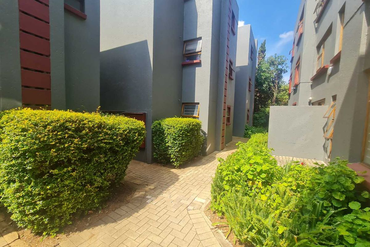 A view of the apartment complex exterior featuring paved walkways and landscaped garden areas between the building blocks.