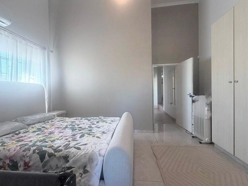 Spacious bedroom featuring neutral walls, tiled flooring, built-in wardrobe storage, and an integrated air conditioning unit.
