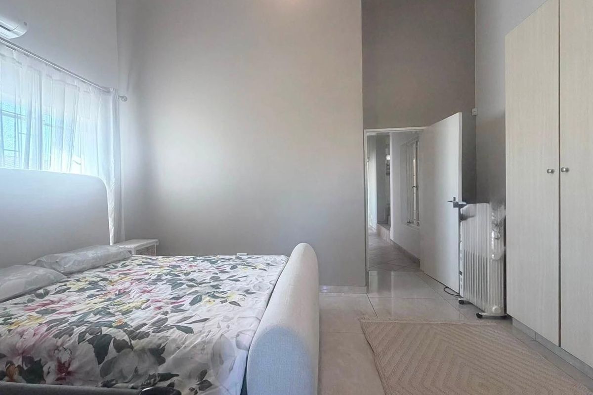 Spacious bedroom featuring neutral walls, tiled flooring, built-in wardrobe storage, and an integrated air conditioning unit.