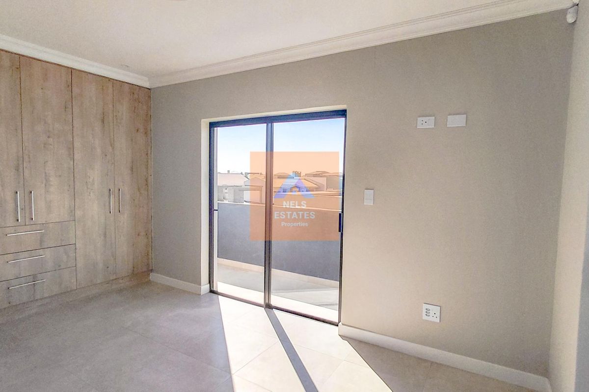 A bright bedroom featuring built-in wooden cabinetry, tiled flooring, and sliding glass doors that open onto a private balcony.