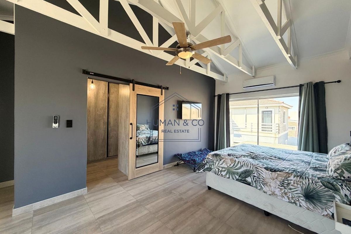 Spacious bedroom featuring vaulted ceilings with exposed trusses, tiled flooring, a ceiling fan, air conditioning unit, and a sliding barn door.