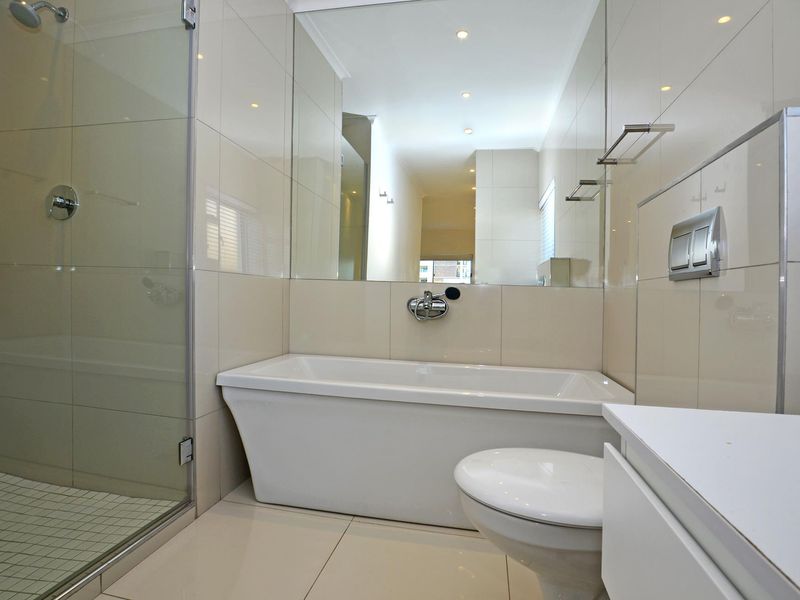 Modern bathroom featuring a sleek freestanding bathtub, glass-enclosed shower, wall-mounted toilet, and large wall mirror with neutral tiled finishes.