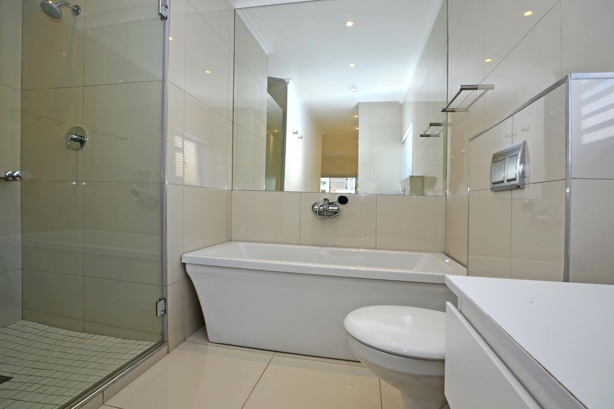Modern bathroom featuring a sleek freestanding bathtub, glass-enclosed shower, wall-mounted toilet, and large wall mirror with neutral tiled finishes.