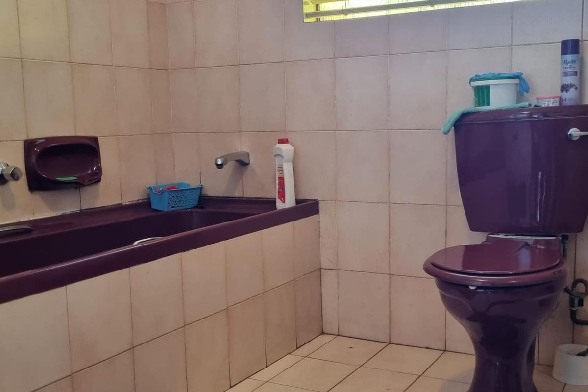 A dated bathroom featuring a dark purple bathtub and matching toilet, complemented by neutral wall and floor tiling.