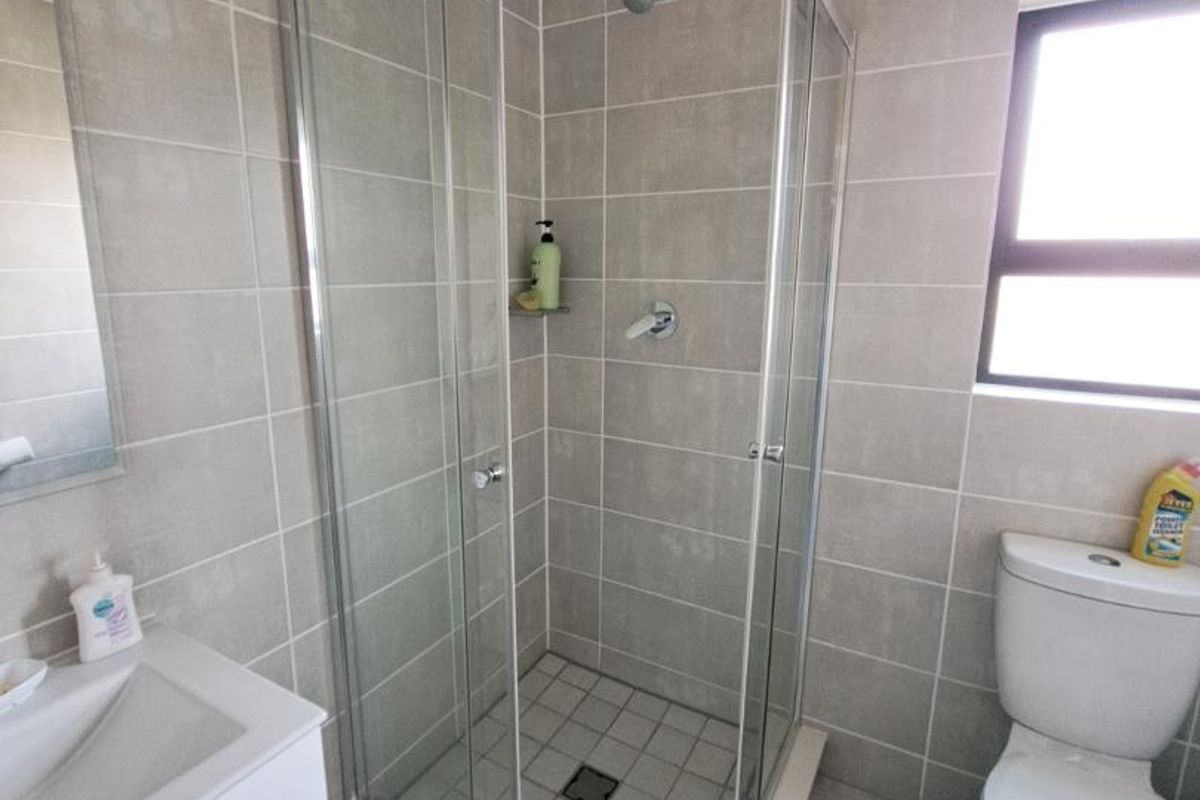 Modern bathroom featuring a glass shower enclosure, vanity basin, and toilet with neutral wall and floor tiling.