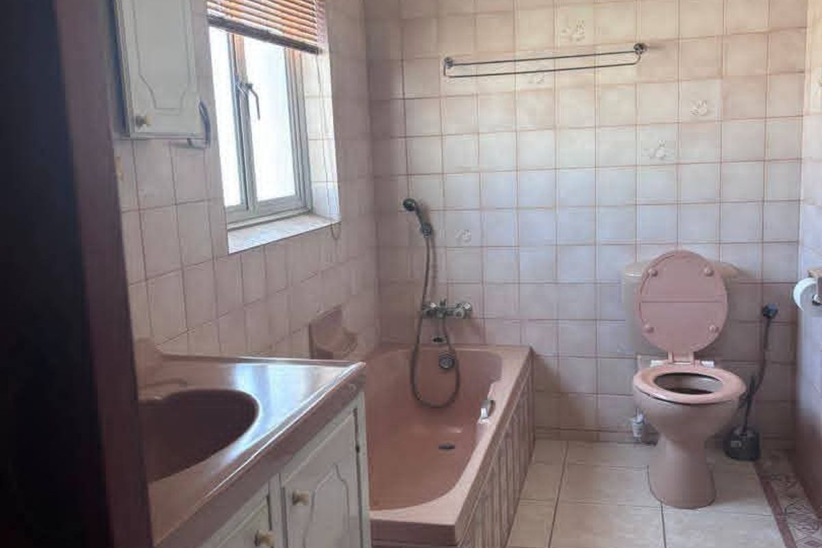 A dated bathroom featuring a pink bathtub and toilet suite, tiled walls and flooring, and a built-in vanity unit.