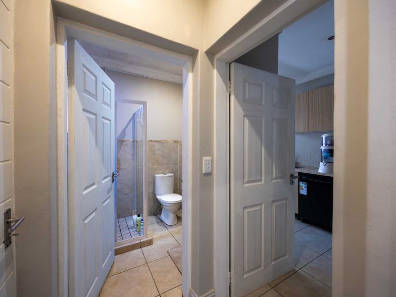A hallway providing access to a bathroom with a shower and toilet, and a kitchen area with built-in cabinetry.