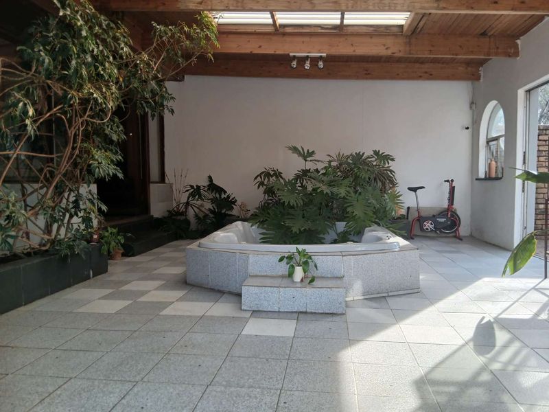 Covered patio area featuring a built-in spa, tiled flooring, and an exposed timber beam ceiling with a skylight.
