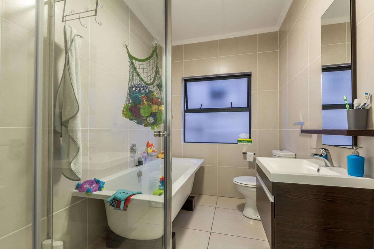 A modern bathroom featuring a bathtub, a glass-enclosed shower, a vanity with a basin, and a toilet, finished with neutral wall and floor tiles.