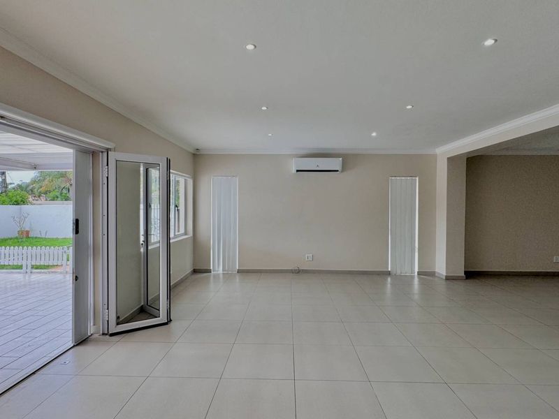 Spacious, light-filled living area featuring neutral tiled flooring, recessed lighting, a wall-mounted air conditioner, and bi-fold doors opening onto an outdoor patio.
