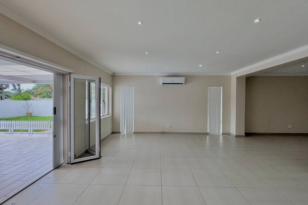 Spacious, light-filled living area featuring neutral tiled flooring, recessed lighting, a wall-mounted air conditioner, and bi-fold doors opening onto an outdoor patio.
