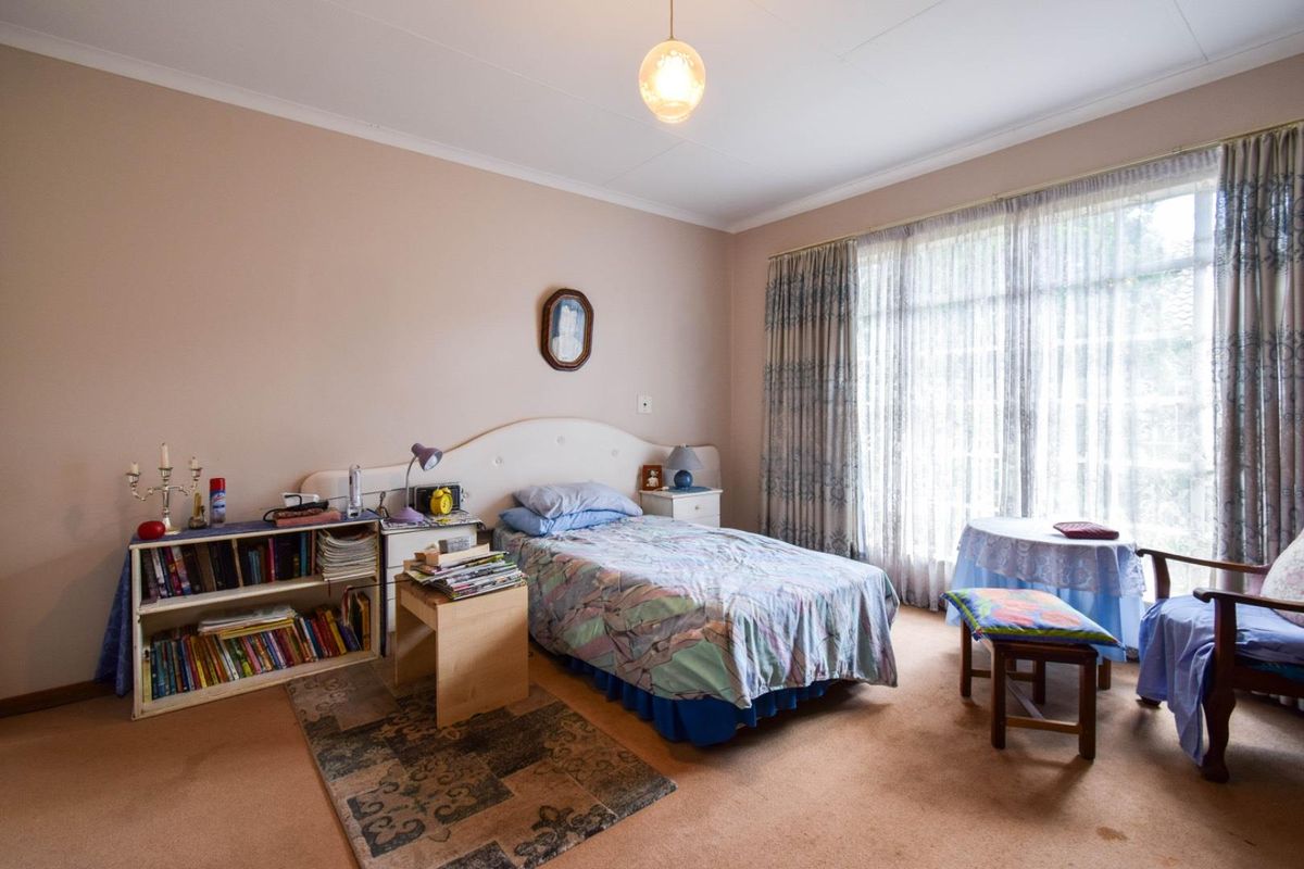 A well-lit bedroom featuring neutral wall tones, carpeted flooring, and large windows with curtains, providing a comfortable and functional living space.
