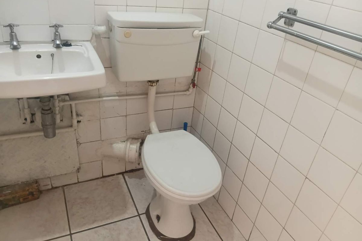 A dated bathroom featuring a standard pedestal basin and toilet with white wall tiling, requiring modernization and cosmetic updates to improve the overall finish.