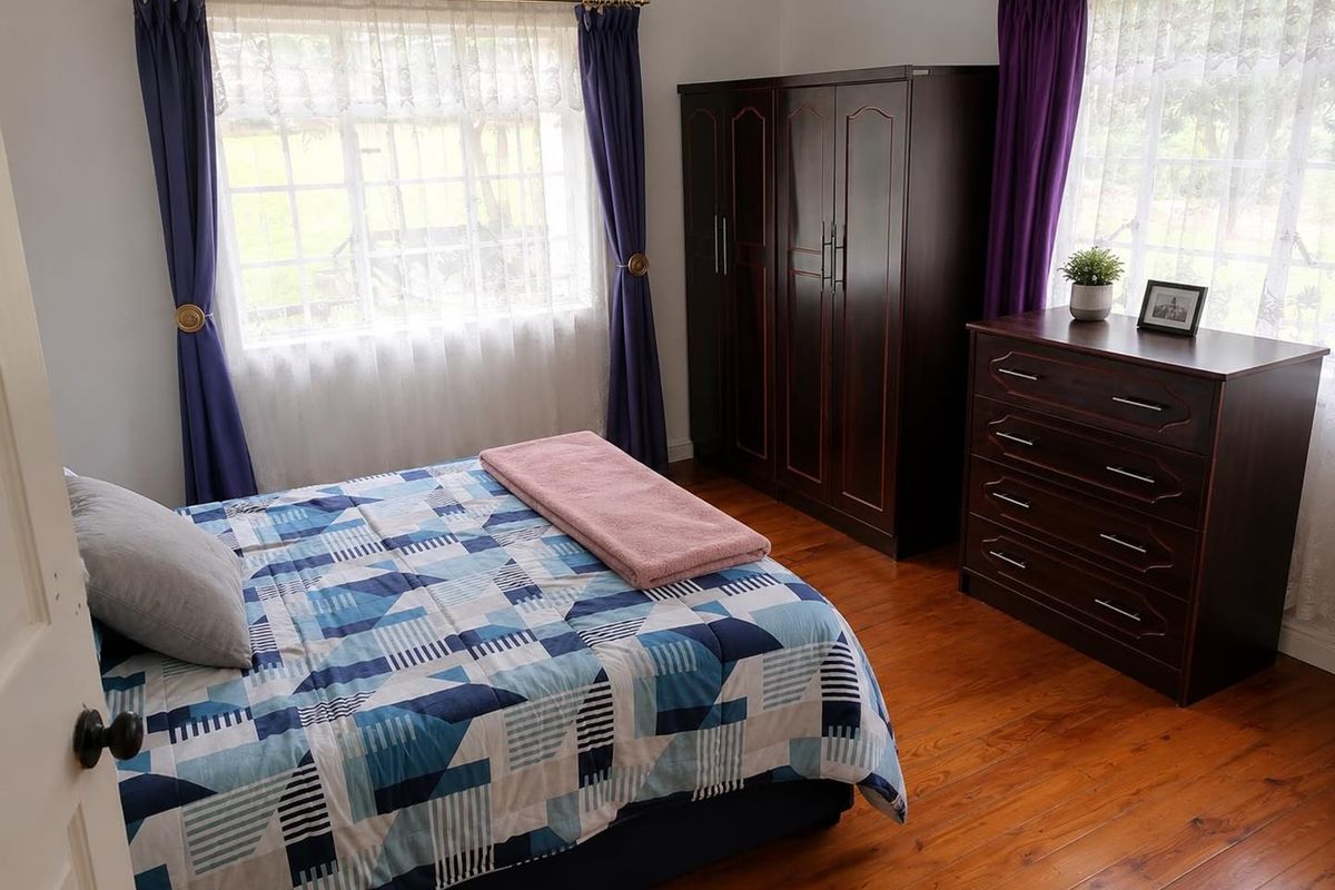 A well-lit bedroom featuring warm wooden flooring and dual windows with curtain rods, offering a comfortable and functional living space.