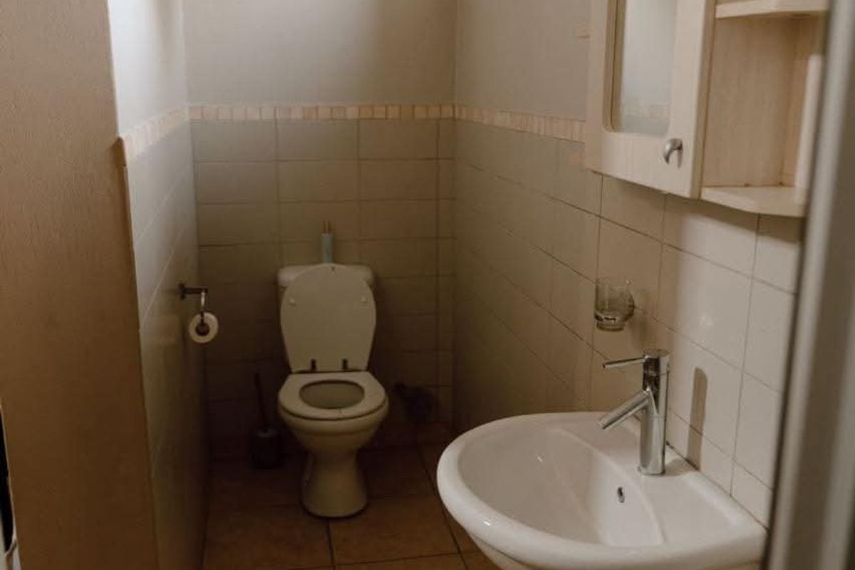 A functional guest bathroom featuring a pedestal basin, toilet, and neutral wall tiling with a wall-mounted medicine cabinet.